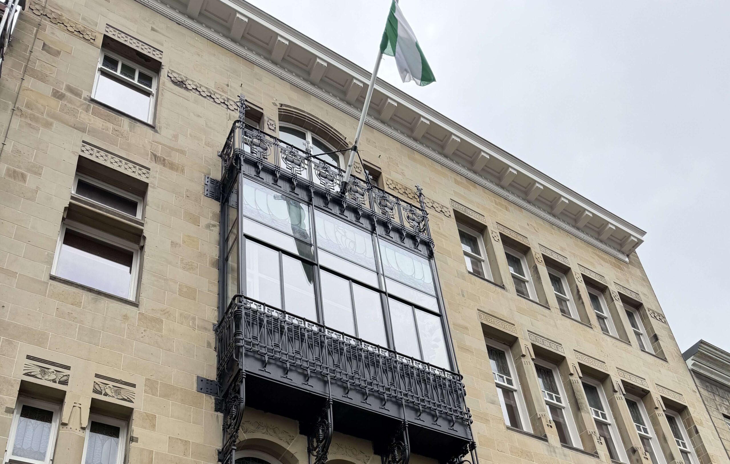 Historische gevel van een rijksmonument met sierlijk zwart balkon en glazen pui